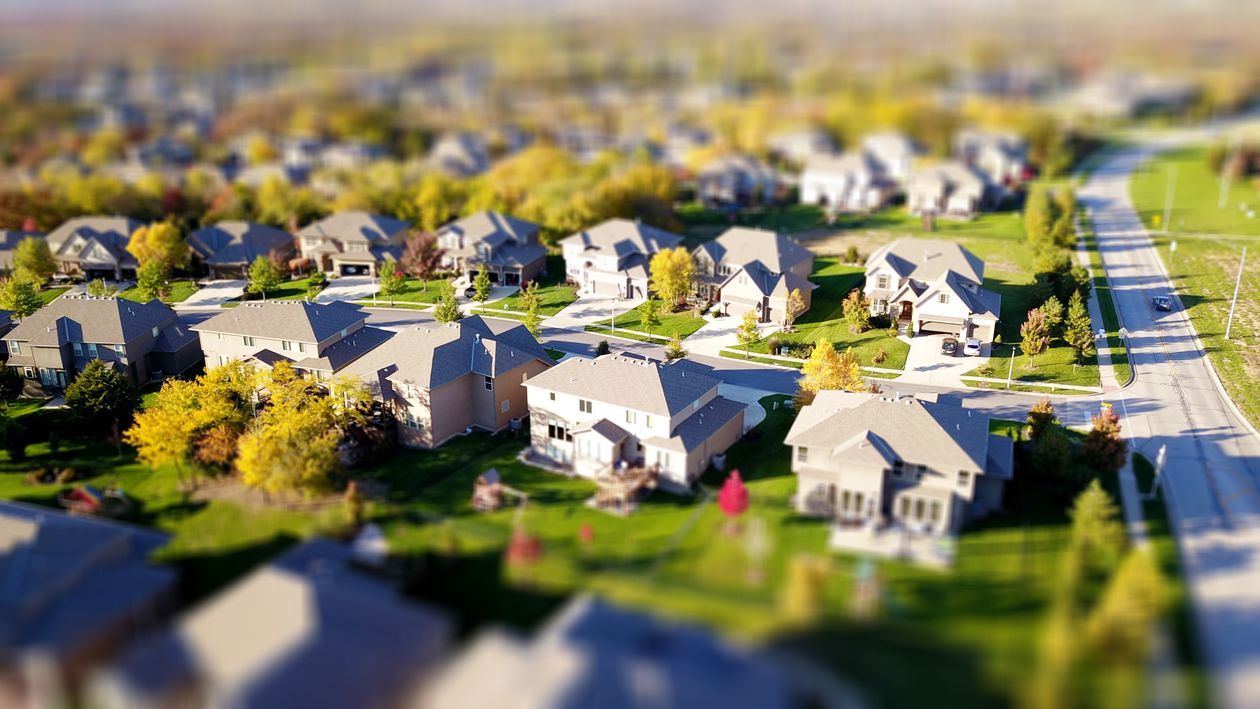 A person holds a digital tablet displaying a map, with a blurred background of a modern residential neighborhood, illustrating the concept of hyper-local SEO targeting.