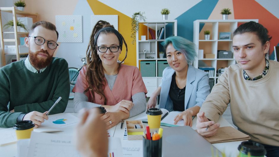 Diverse group of professional real estate agents sit around a modern conference table, actively collaborating on plans for...